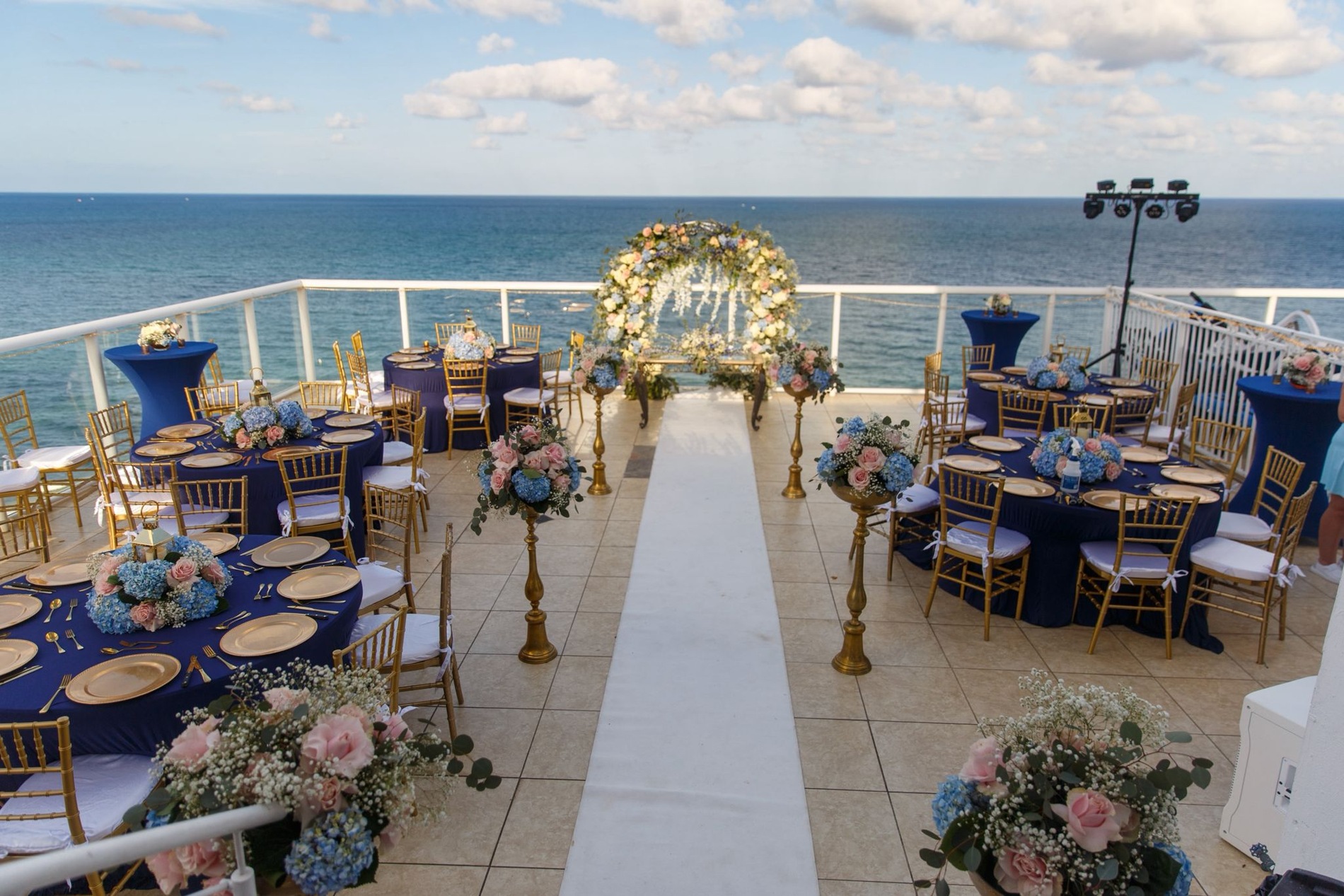Real oceanfront penthouse wedding setup with a floral arch, navy table linens and gold chairs overlooking the sea