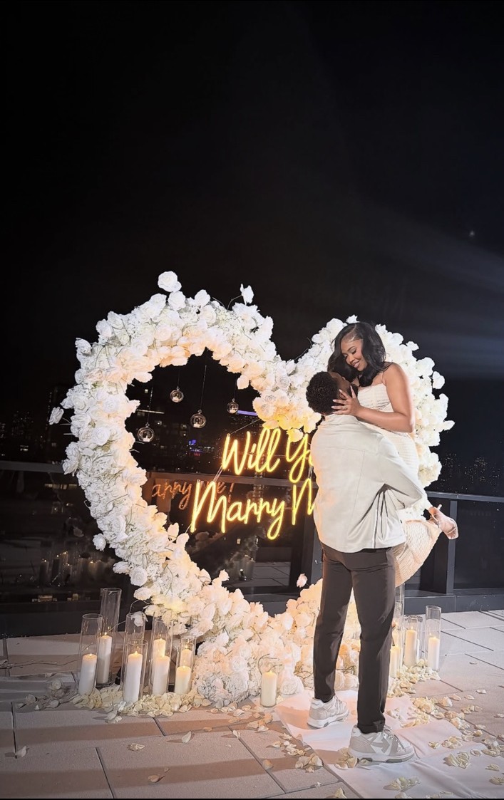 A white floral heart and warm candlelight frame a joyful proposal moment.
